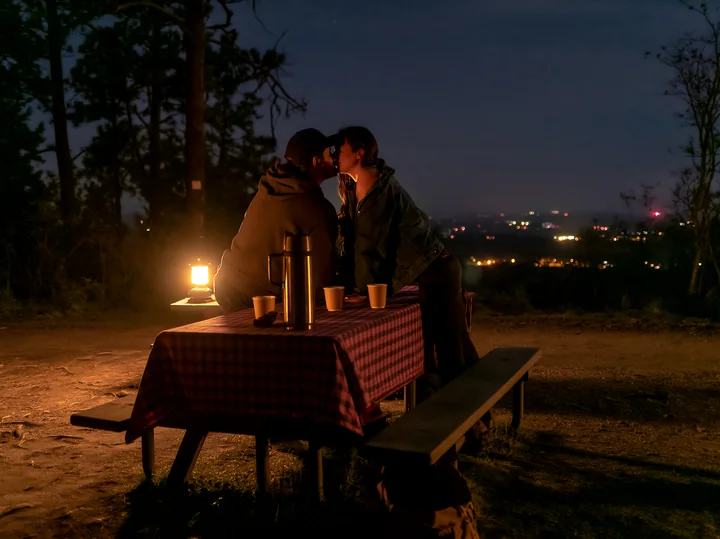 A couple shares a kiss on a mountain overlook while illuminated by a lantern.
