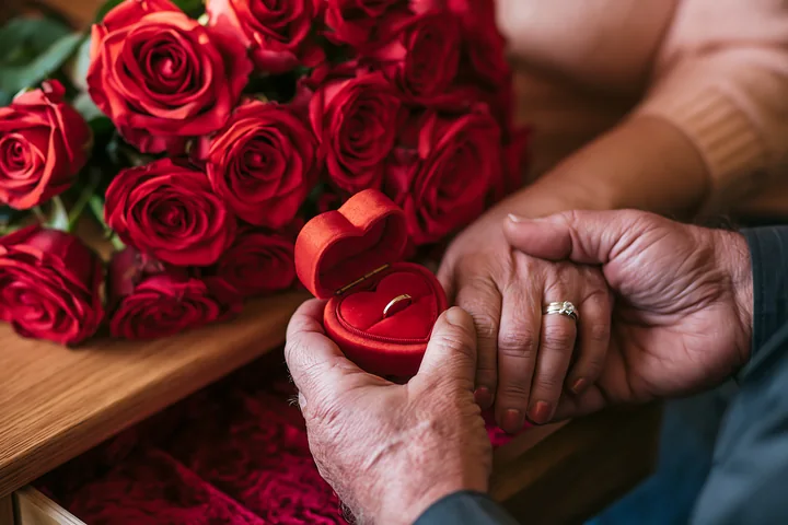 A hand holds a heart-shaped ring box while another hand reaches out.