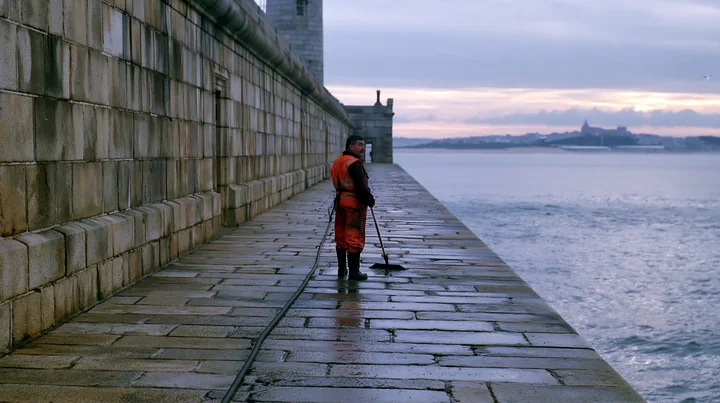 A lighthouse maintenance worker at work cleans the stone walkway along the sea.