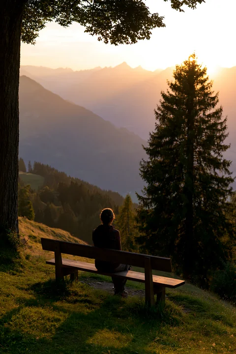 A person sits on a bench, looking out over the Swiss landscape in golden light during sunset.