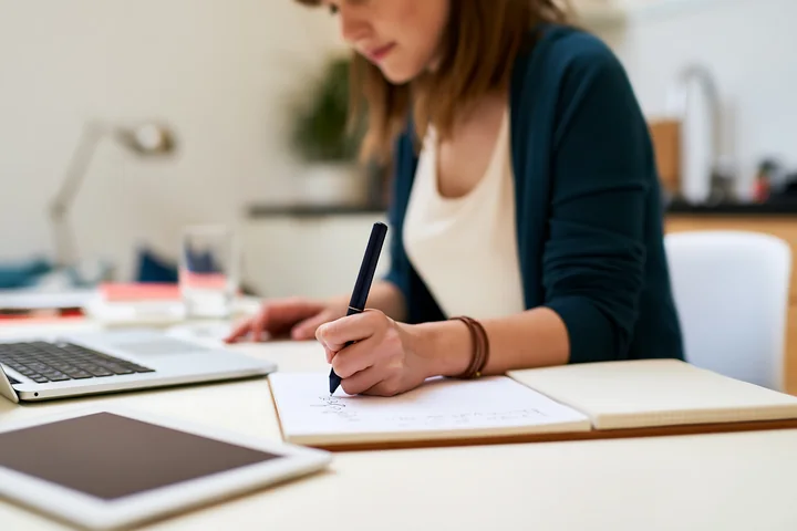 A person writes a gift list on paper while seated at a desk.