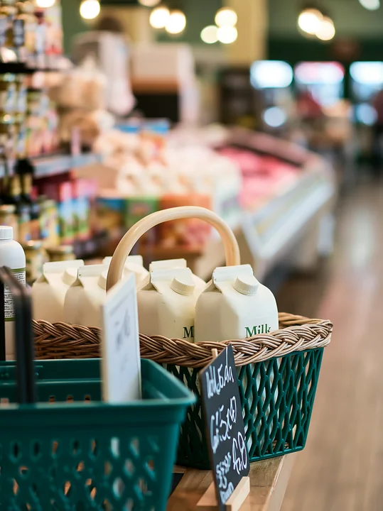 A shopping basket contains milk cartons at a market filled with various goods.