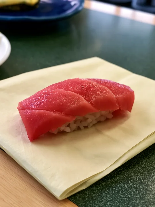 A single sushi piece with colorful fish topping rests on a light-colored plate.