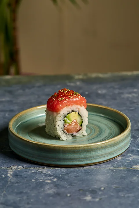 A single sushi roll on ceramic plate features a filling of cucumber and salmon.