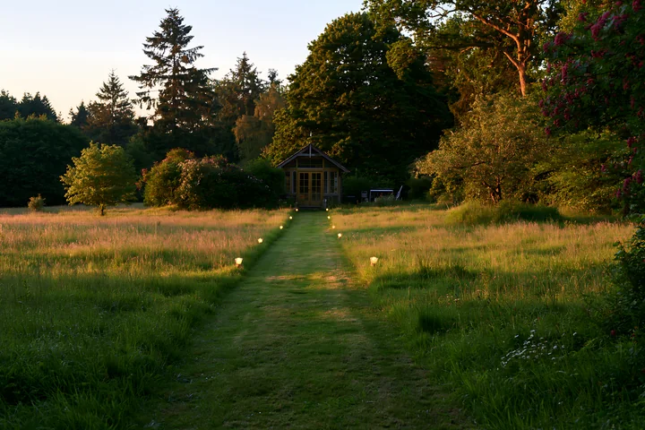 A vacant garden house is illuminated by pathway lights along a green path.