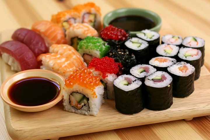A variety of sushi types are displayed on a wooden platter, featuring colorful rolls and sauces.