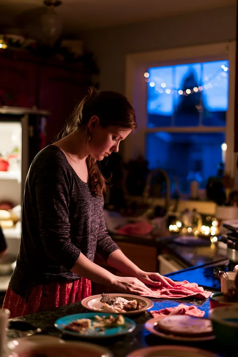 A woman is cleaning up in a cozy kitchen after a festive holiday celebration.