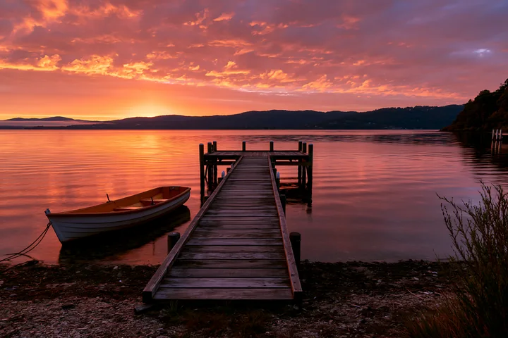 A wooden dock extends into calm waters at sunset, with a small boat resting nearby.