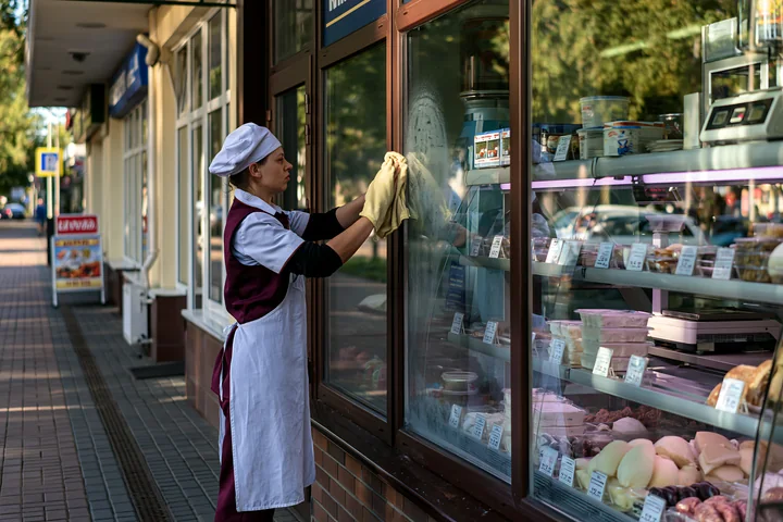 A worker wipes the glass display of a dairy products shop on a pedestrian street.