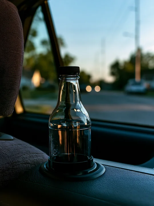 An empty bottle sits in a car cup holder as evening light filters through the window.
