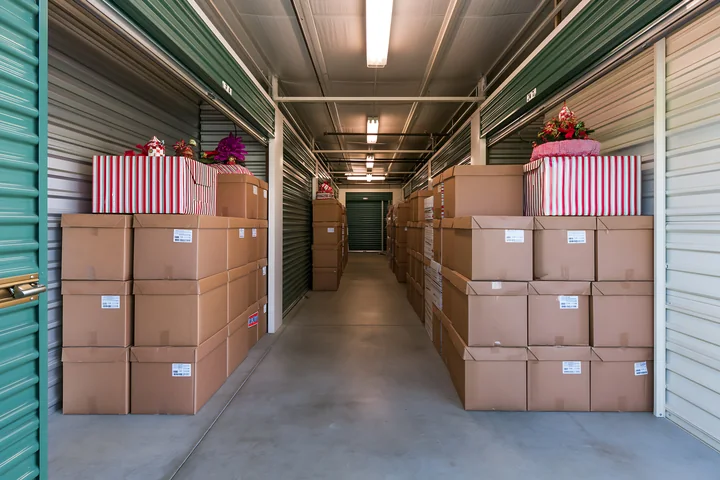 Cardboard boxes packed with Christmas decorations line a brightly lit self-storage corridor.