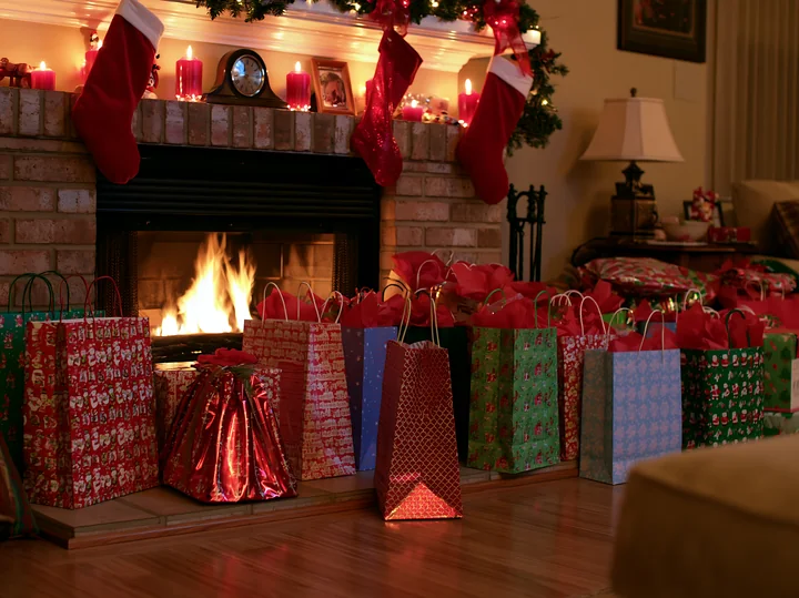Colorful holiday shopping bags fill the area beside a fireplace decorated with stockings and candles.