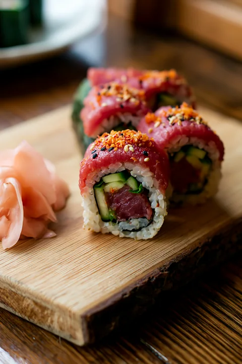 Fresh spicy tuna rolls are displayed on a wooden board alongside pickled ginger.