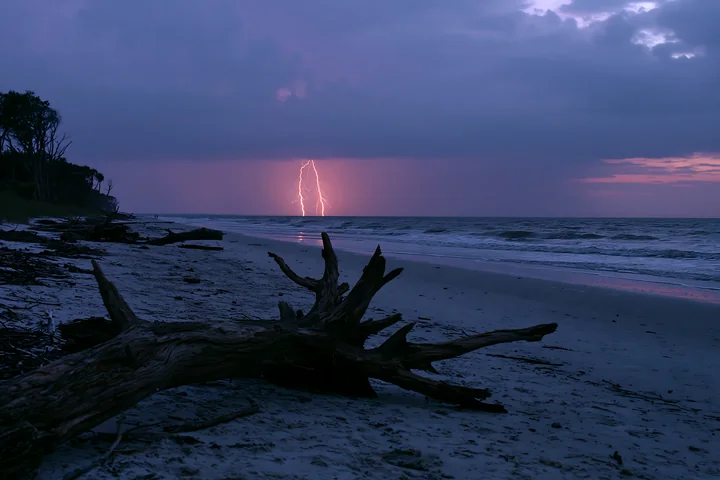 Lightning strikes over the ocean as dark clouds gather at dusk.