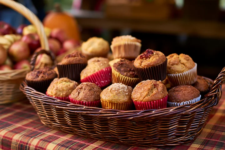 Muffins of various flavors are arranged in a basket at a seasonal market setting.