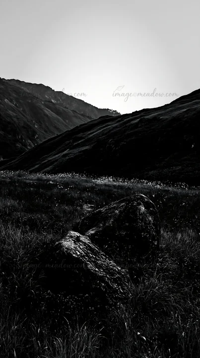 A granite boulder rests in a meadow in Nagano. The surrounding grass is green, and hills rise in the background during twilight hours. Presented as a premium hi