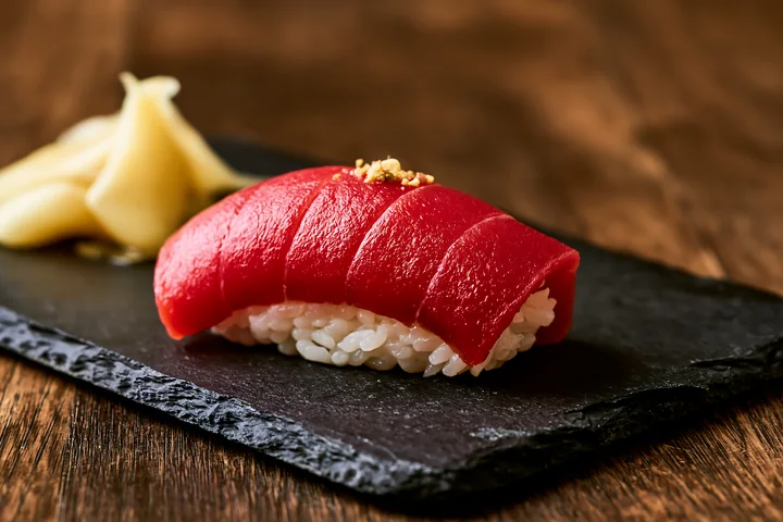 One sushi piece with pickled ginger features bright red tuna atop white rice.