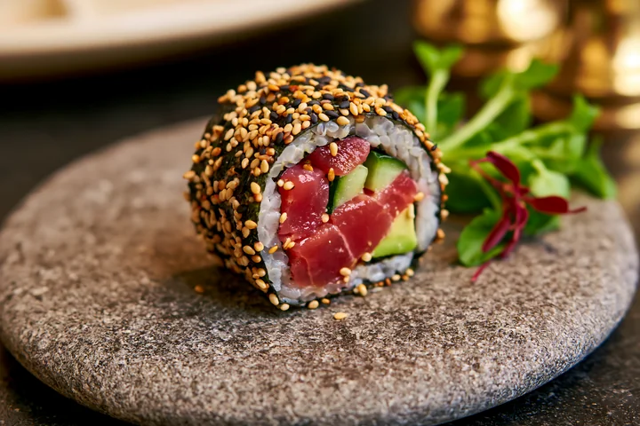 One tuna roll slice with sesame coating sits on a gray stone plate.