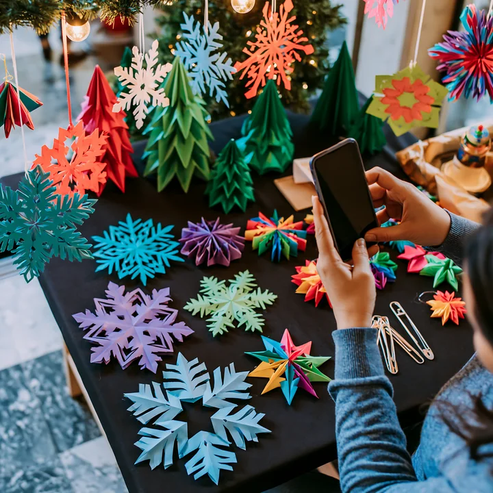 Person photographs colorful handmade paper Christmas ornaments at a festive market stall.