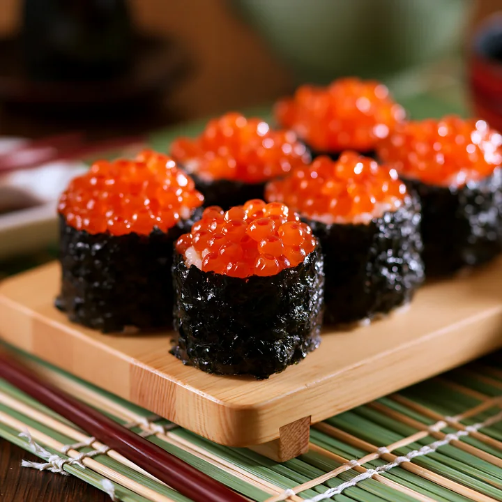 Sushi rolls filled with rice and vegetables, topped with vibrant ikura salmon roe, are served on a wooden plate.