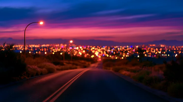 The scene shows a winding road leading to a city illuminated by colorful lights at dusk, with a colorful sky transitioning from day to night.