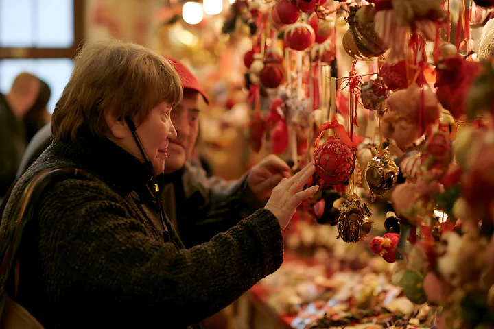 Two customers admire and choose handmade ornaments at a Christmas market stall.