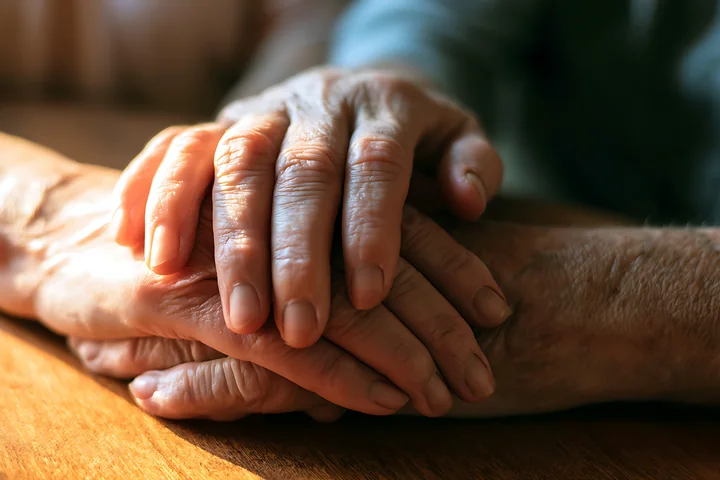 Two hands are intertwined on a table during a hospice visit, showing connection and support.