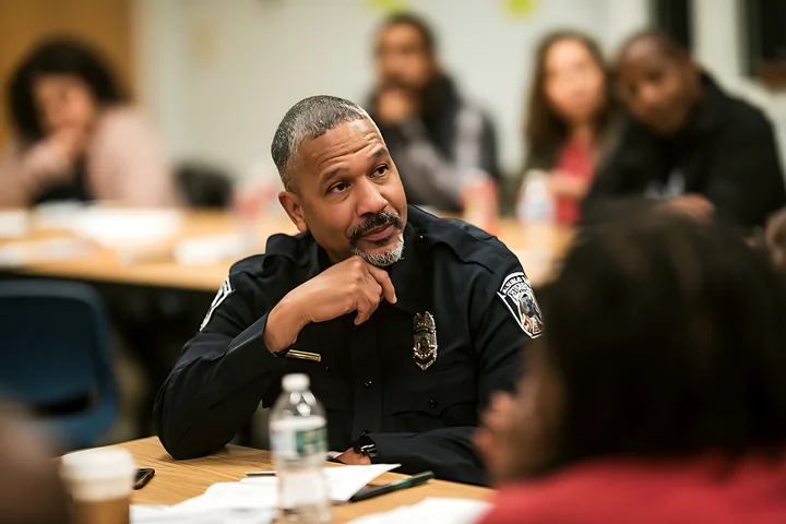 Uniformed police officer listens at a conference table during a civilian oversight meeting.