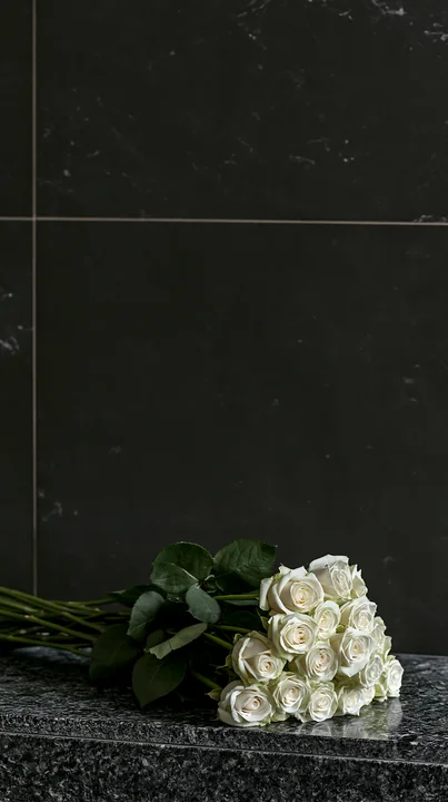 White roses rest on dark stone beneath a black tiled background, leaving wide empty space above for copy.