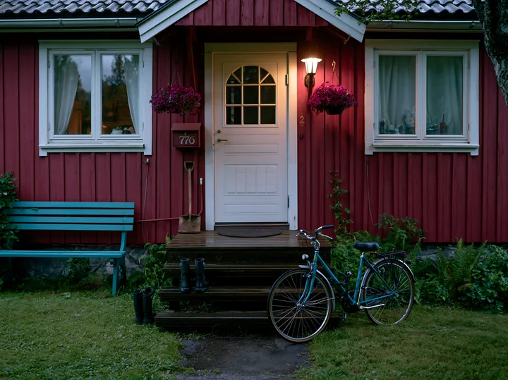 A bicycle leans against the steps of a country home surrounded by greenery.