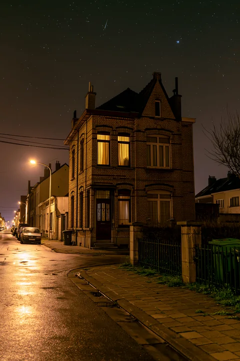 A brick house stands in a quiet neighborhood as a meteor shower illuminates the night sky.