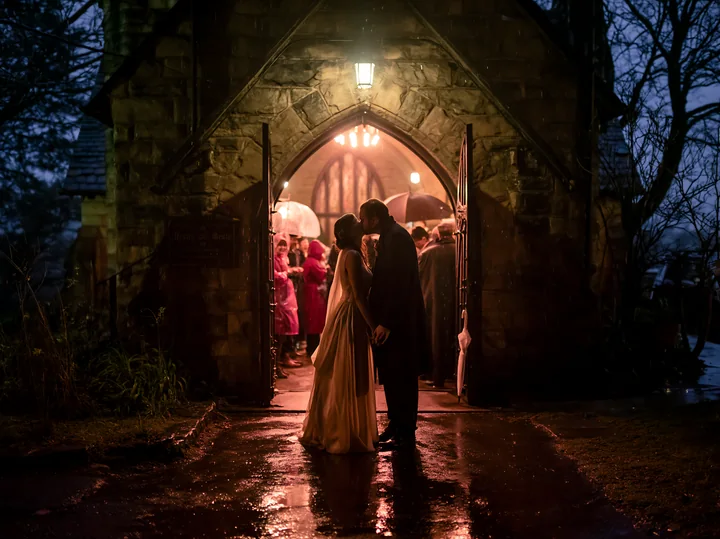 A bride and groom share a kiss outside a chapel after their wedding ceremony.