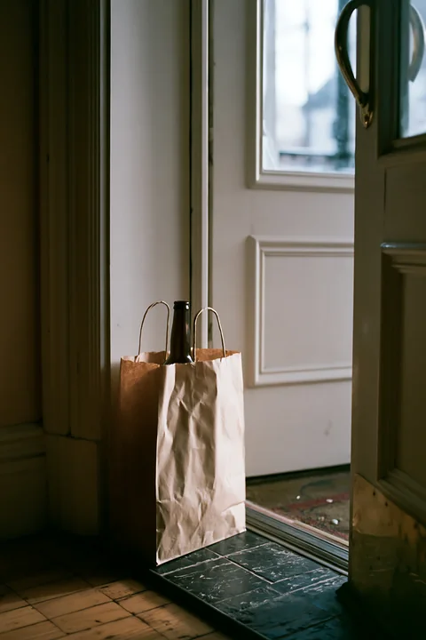 A brown paper bag leans against the door with an empty bottle after party.