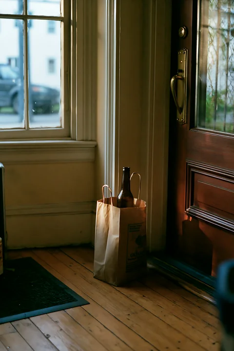 A brown paper bag sits by the door with an empty bottle after party inside.
