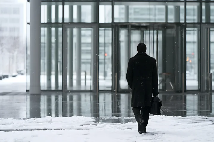 A businessman walks toward a modern office entrance in snowy weather.