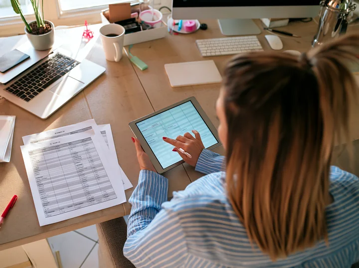 A businesswoman uses a tablet to manage a project timeline at her desk.