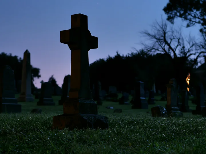 A cemetery dedicated to soldiers features dark gravestones and a cross in the foreground with a night sky filled with stars.