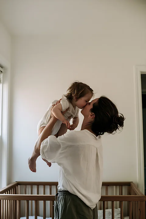 A child kisses a parent while being held in a nursery.