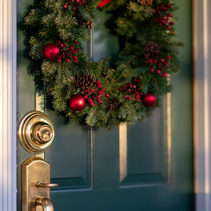 A Christmas wreath made of pine and decorated with red ornaments is hung on a green apartment door.