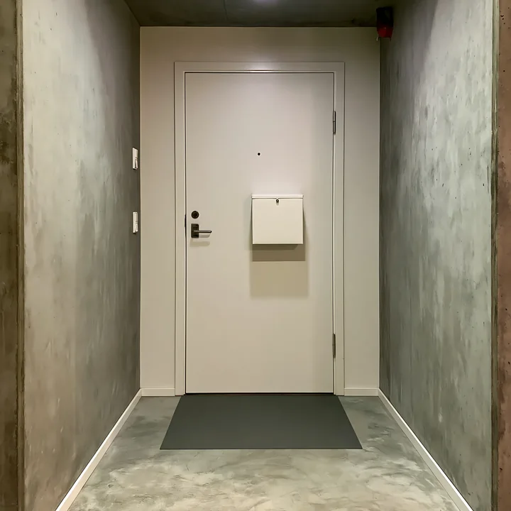 A clean and modern apartment doorstep features a white door and an insulated milk delivery box mounted on the wall.