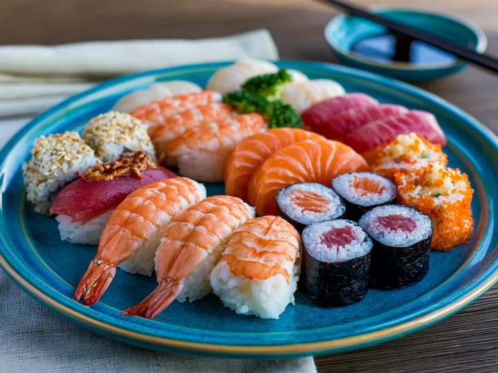 A close-up view of a modern sushi presentation featuring sushi rolls, nigiri, and sashimi arranged on a blue plate.