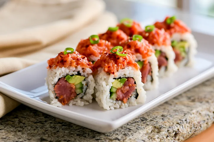 A close-up view of a plate containing several spicy tuna rolls, showing layers of sushi rice, avocado, and topped with spicy tuna.