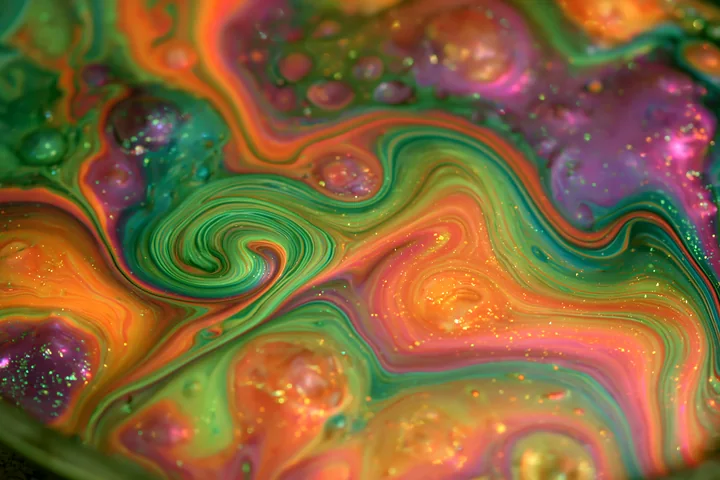 A colorful abstract swirl glittering pattern showcases vibrant greens, oranges, and purples with swirling shapes and sparkling dots.