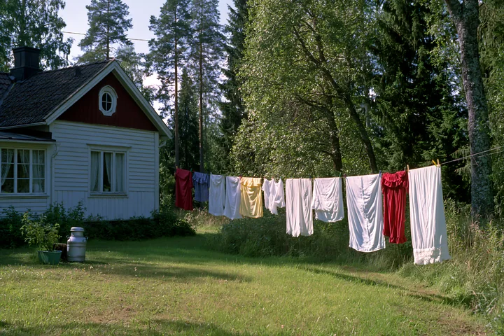 A cottage near forest edge features colorful laundry drying on a line.