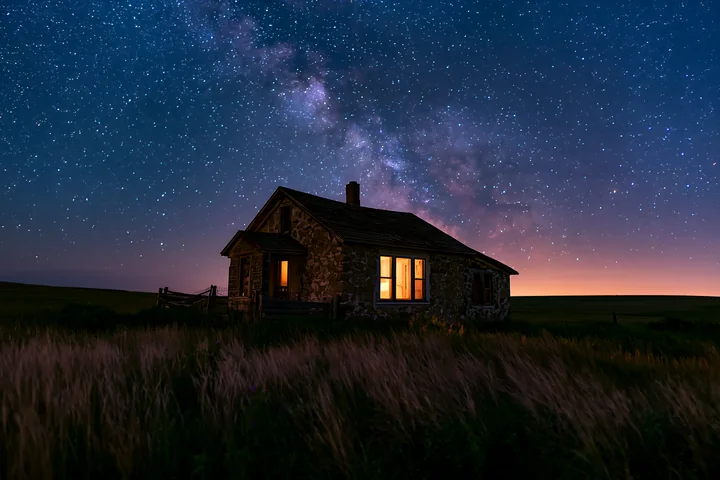 A country house stands in a rural setting under a clear night sky filled with stars and the milky way.