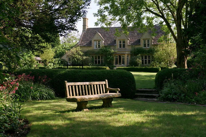 A country house surrounded by hedges stands in a well-kept garden.