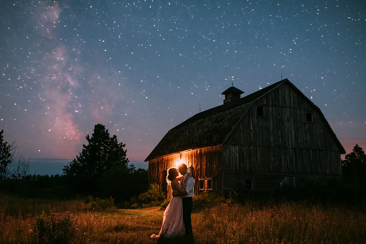 A couple dances together under a starry sky beside an old barn.