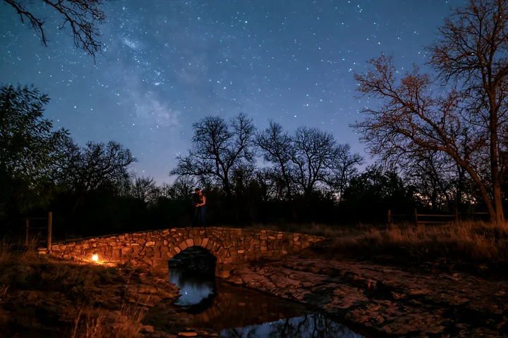 A couple kissing under stars during a romantic date stands on a stone bridge.
