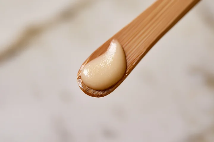 A creamy substance sits on a wooden stick, showcasing a matte texture.