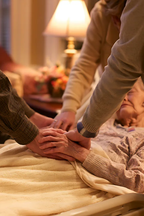 A family gathers around a hospice patient, holding hands to show support and care.